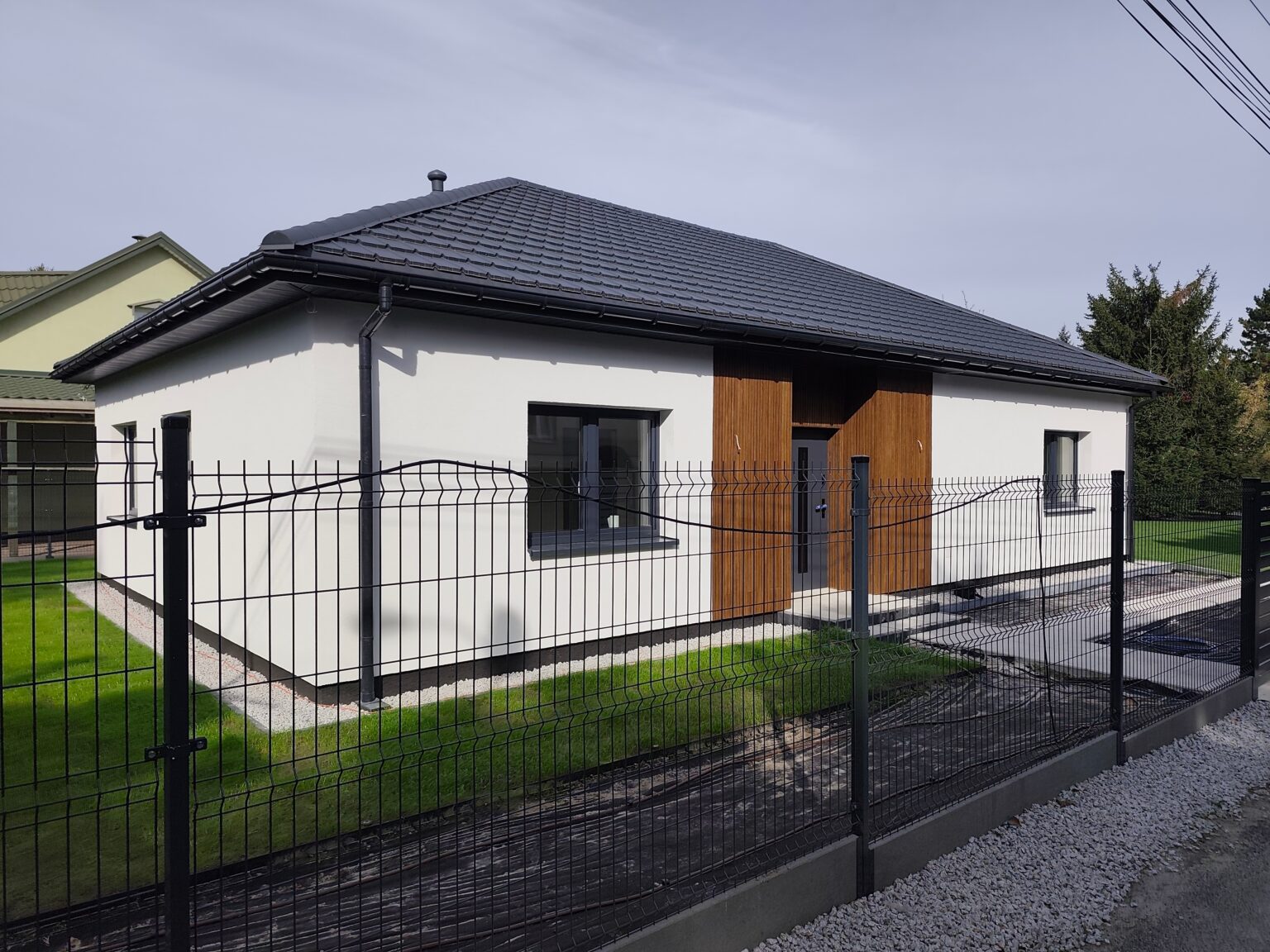 Elewacja frontowa domu 111 m² – biały tynk, grafitowy dach i drewniane okładziny przy wejściu